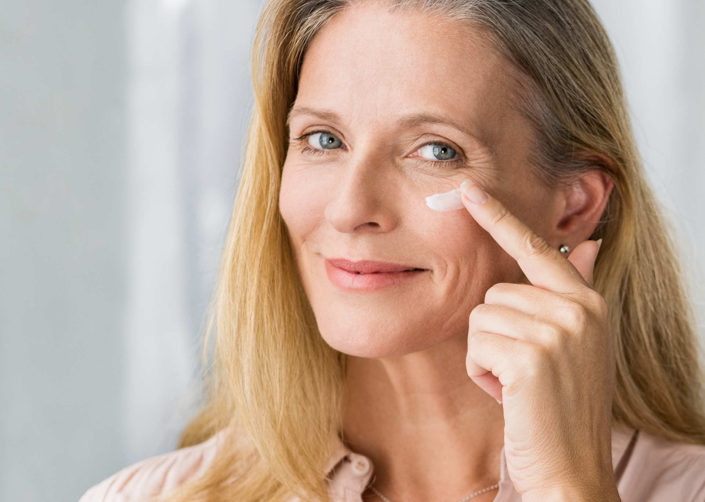 Eine glücklich schauende Frau mittleren Alters streicht sich Creme auf die Wange