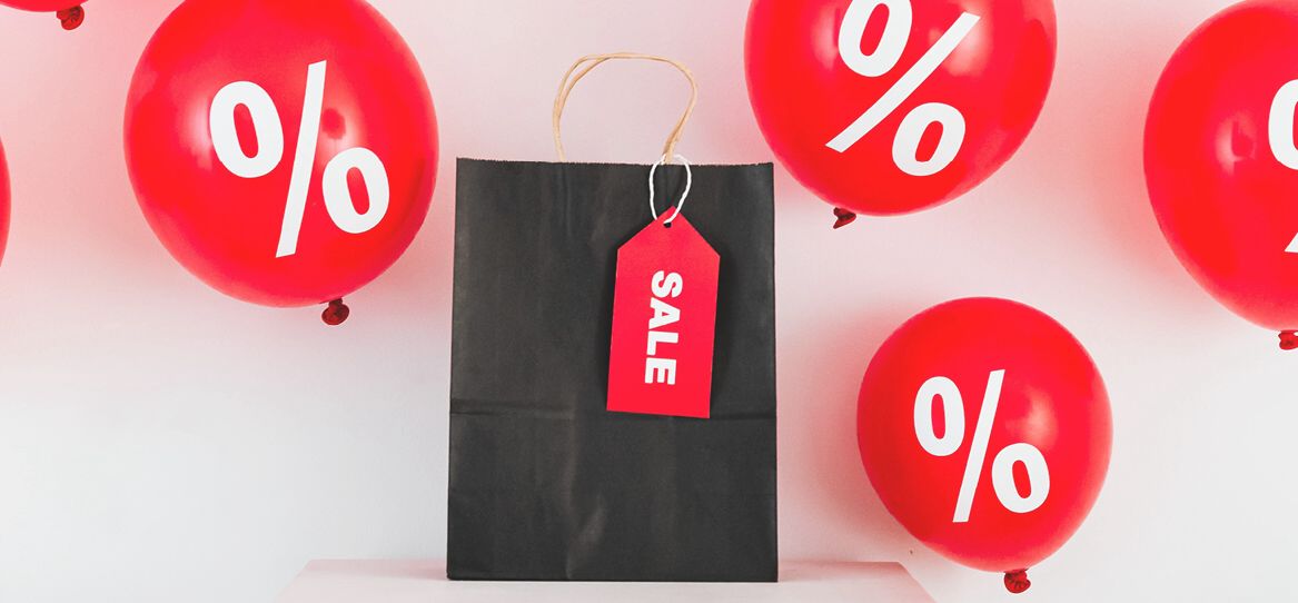 Eine Einkaufstüte mit einem Sale Schildchen sowie mehrere rote Ballons mit einem weißen Prozenzeichen Aufdruck