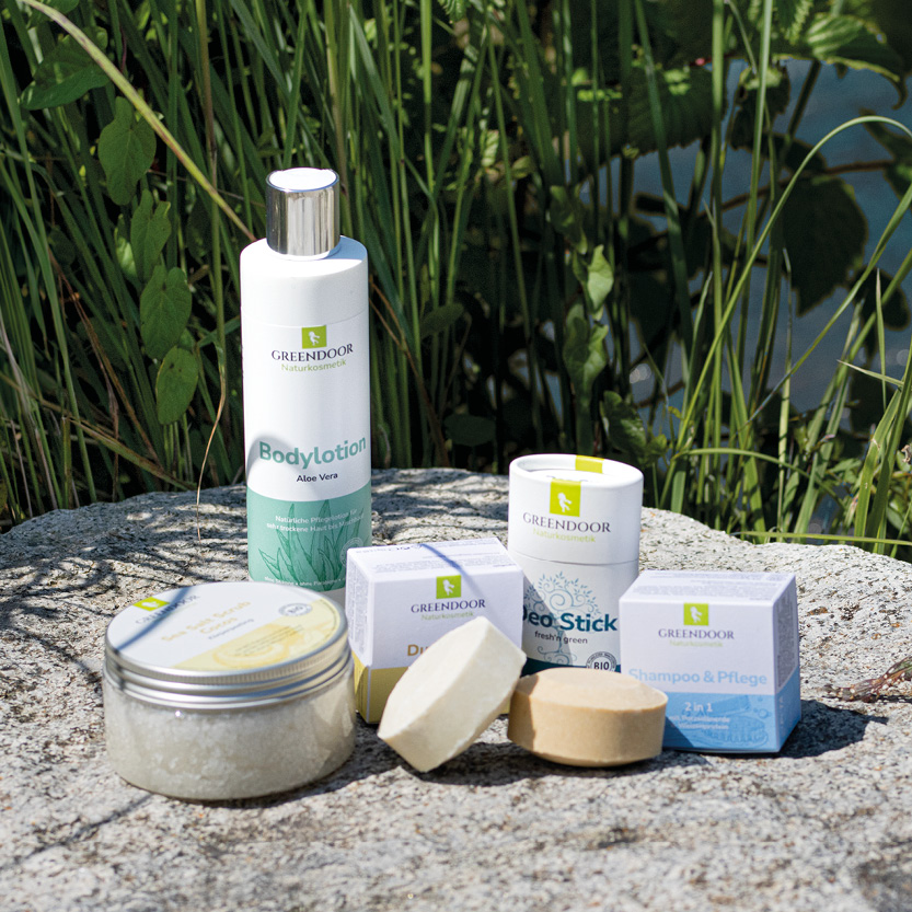 Bildmaterial_Blog_Sommerprodukte Verschiedene Greendoor Produkte die auf einem Fels vor einem Gewässer zu sehen sind. Die Sonne scheint