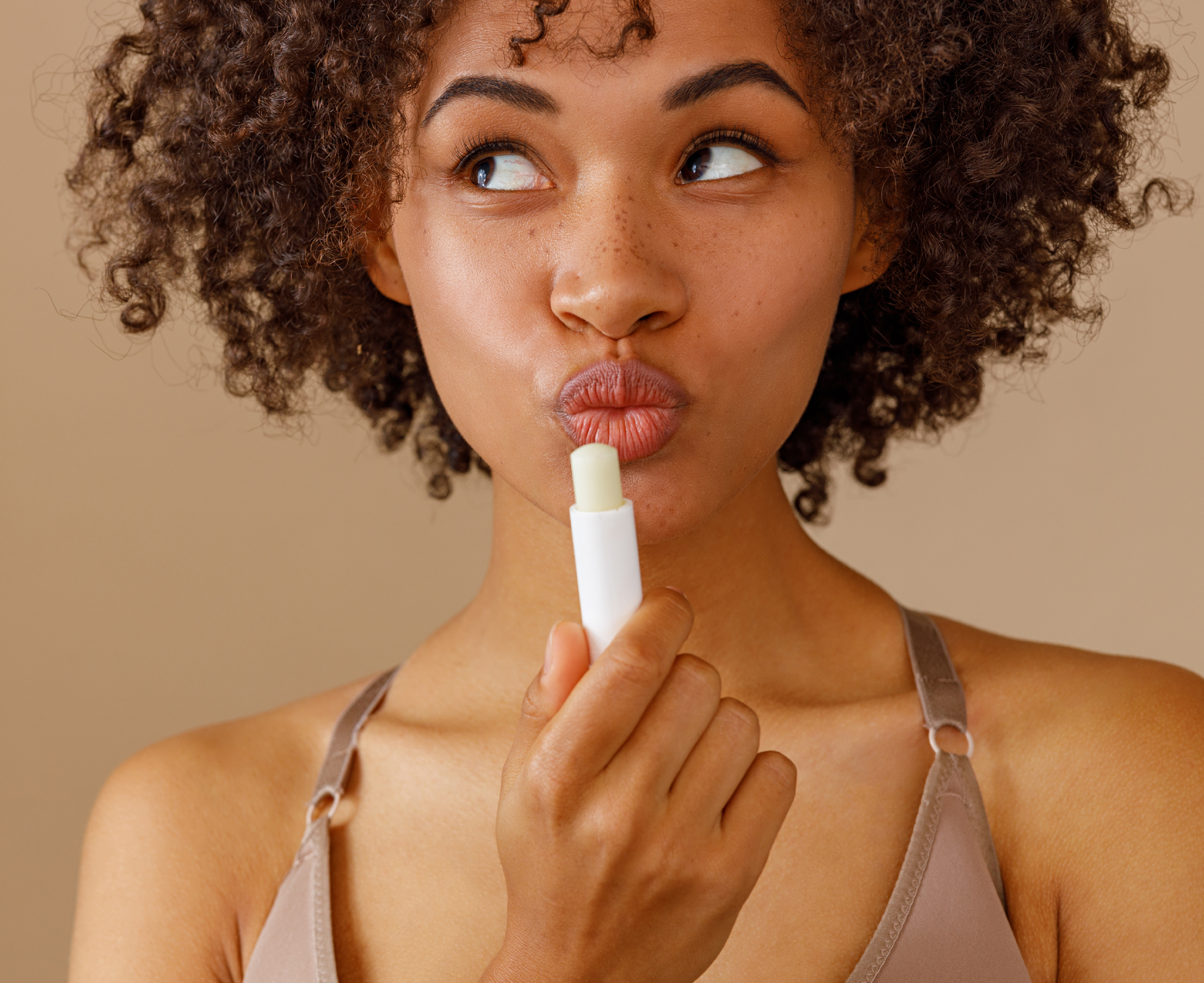 Junge Frau mit Locken cremt sich die Lippen mit einem Lippenpflegestift