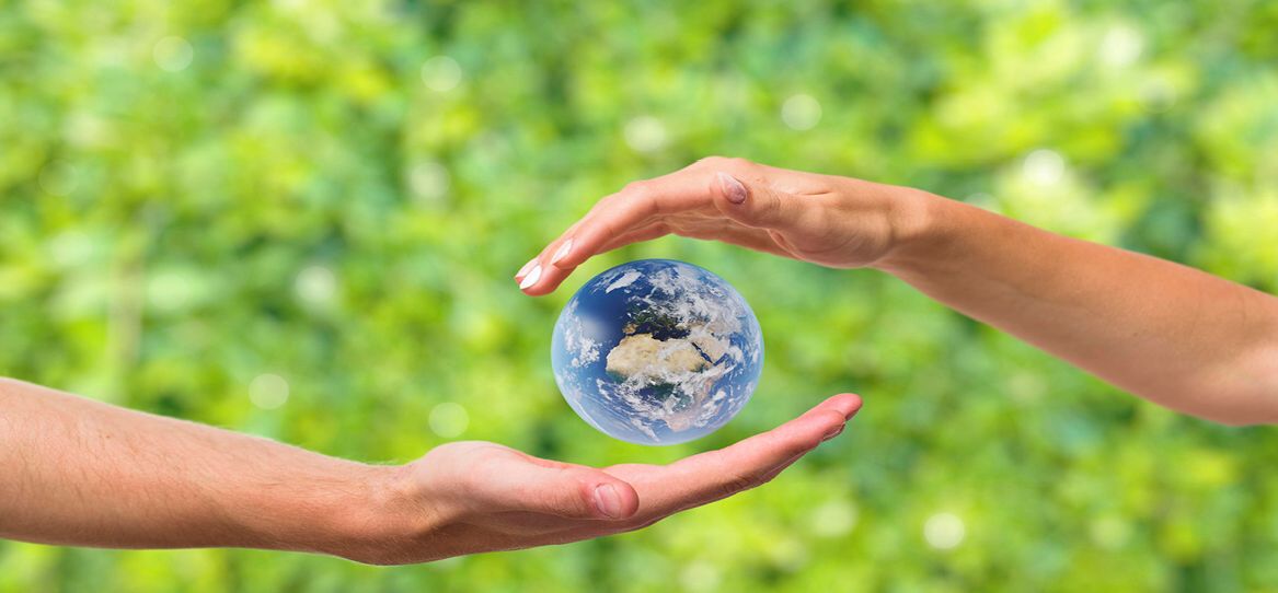 Zwei Hände vor natürlich grünem verschwommenen Hintergrund die symbolisch eine Minierde umschließen