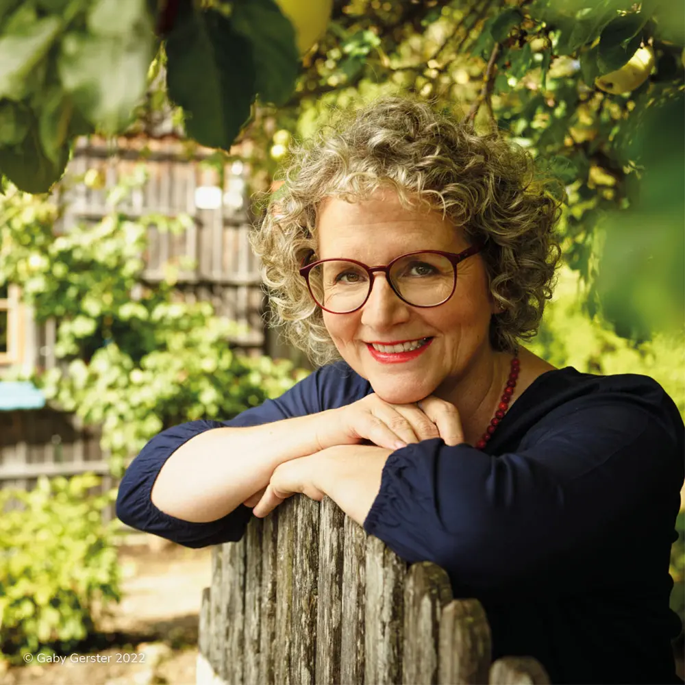 Blog_Bild20a Lächelnde Frau mittleren Alters, die eine Brille trägt in einem grünen Garten